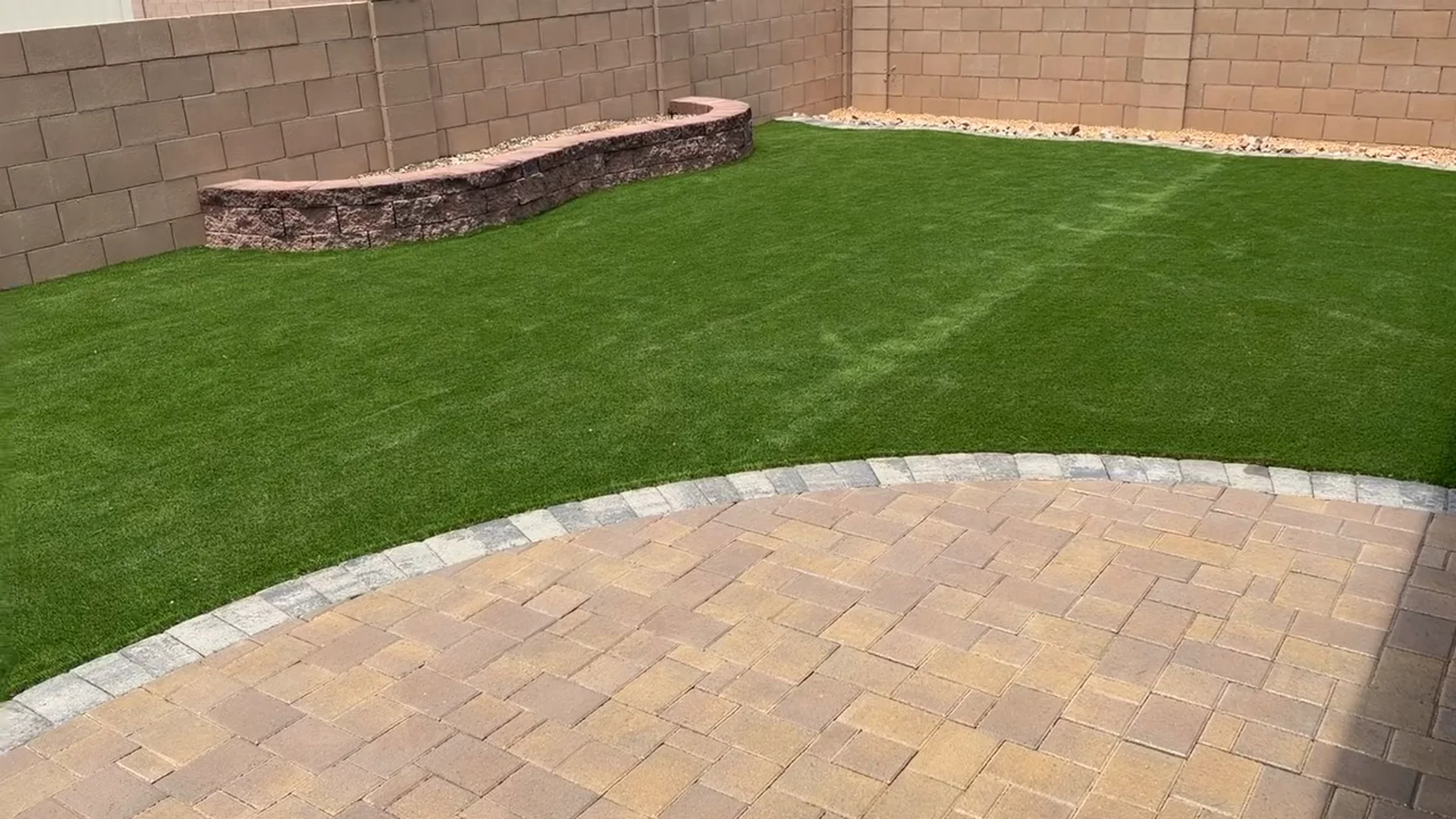 Completed backyard with artificial turf, paver patio, and masonry planter wall